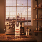 Weiße Kaffeetüte des Cuxhavener Kaffeeroesters mit der Aufschrift Espresso Alte Liebe in Küche mit verschiedenen Kaffeemaschinen vor Fenster Hafenkulisse an der Nordsee 