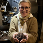Inhaberin präsentiert vor Kaffeeröstmaschine, frisch geröstete Kaffeebohnen.
