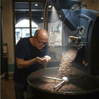 Eigentümer bei der Qualitätsprüfung frisch gerösteter Kaffeebohnen, während diese aus einer Kaffeeröstmaschine fallen