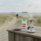 Weiße Kaffeetüte des Cuxhavener Kaffeeroesters mit der Aufschrift Äthiopien Sidamo auf Outdoor-Küche mit frisch gebrühtem Filterkaffe  mit Dünen- und Nordseeblick
