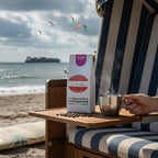 Weiße Kaffeetüte des Cuxhavener Kaffeeroesters mit der Aufschrift Colombia auf Tisch von Strandkorb mit Kaffeetasse und Nordseeblick