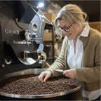 Eigentümerin die frisch geröstete Kaffeebohnen im Cooler einer Kaffeeröstmaschine auf Qualität prüft