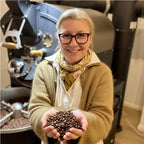 Eigentümerin präsentiert frisch geröstete Kaffeebohnen vor Kaffeeröstmaschine