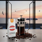 Weiße Kaffeetüte des Cuxhavener Kaffeeroesters mit der Aufschrift Grimmershörner Morgenröte mit French Press und Fenster mit Nordseeblick