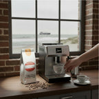 Weiße Kaffeetüte des Cuxhavener Kaffeeroesters mit der Aufschrift Kenya Crema AB  mit Kaffeemaschine in Küche und Fenster mit Nordseeblick
