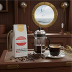 Weiße Kaffeetüte des Cuxhavener Kaffeeroesters mit der Aufschrift Lotsenmischung  mit French Press und Kaffeetasse in Schiffskombüse und Bullauge mit Nordseeblick
