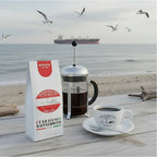 Weiße Kaffeetüte des Cuxhavener Kaffeeroesters mit der Aufschrift Nicaragua   mit French Press auf Bar vor Nordseestrand