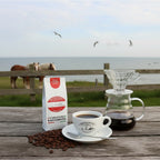 Weiße Kaffeetüte des Cuxhavener Kaffeeroesters mit der Aufschrift Papua Neuguinea auf Gartentisch mit Blick auf Pferdekoppel und Nordsee