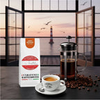 Weiße Kaffeetüte des Cuxhavener Kaffeeroesters mit der Aufschrift Kenya Espresso auf Küchentheke  mit frisch gebrühtem Espresso und French Press vor Fenster mit Nordseeblick